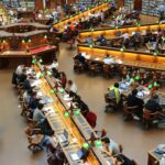 A lively university library scene with students studying diligently at wooden desks.