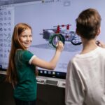 Saat Silicon Valley dan AI Membutuhkan Anak Humaniora Two children interacting with a digital screen in a classroom setting, learning through technology.